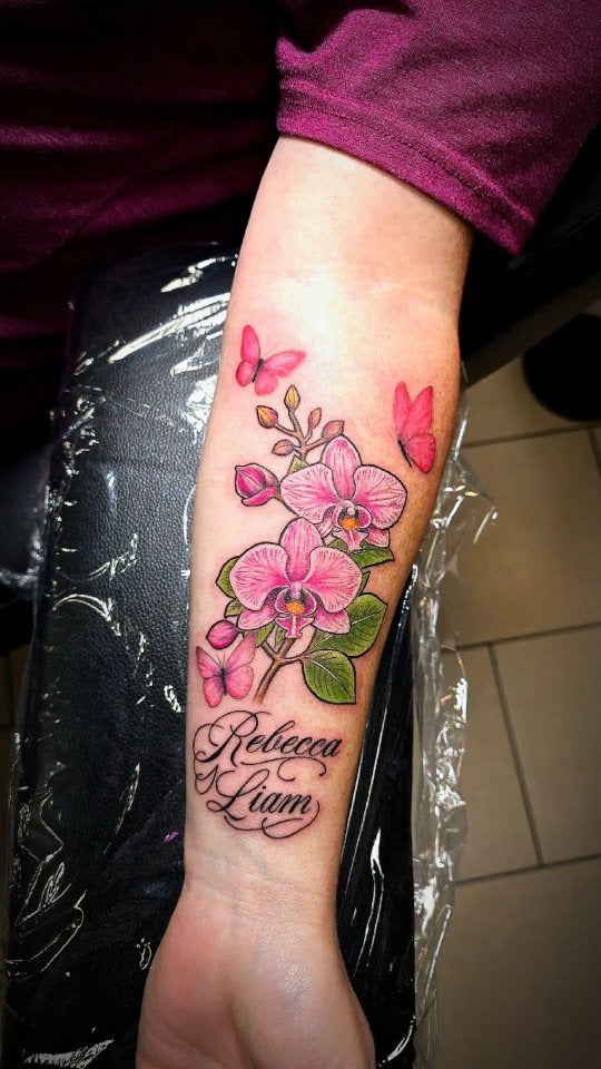 Tattoo by Angel at Z-Edge Gulf Gate: pink orchids and butterflies with script names on the forearm