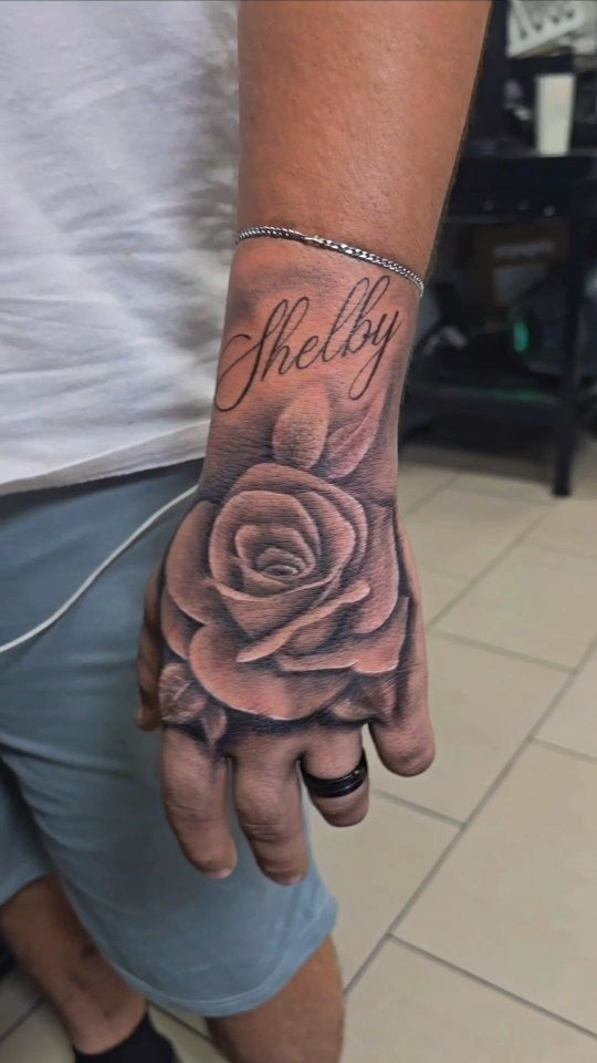 Tattoo by Angel at Z-Edge Gulf Gate: black and grey rose on the hand with script