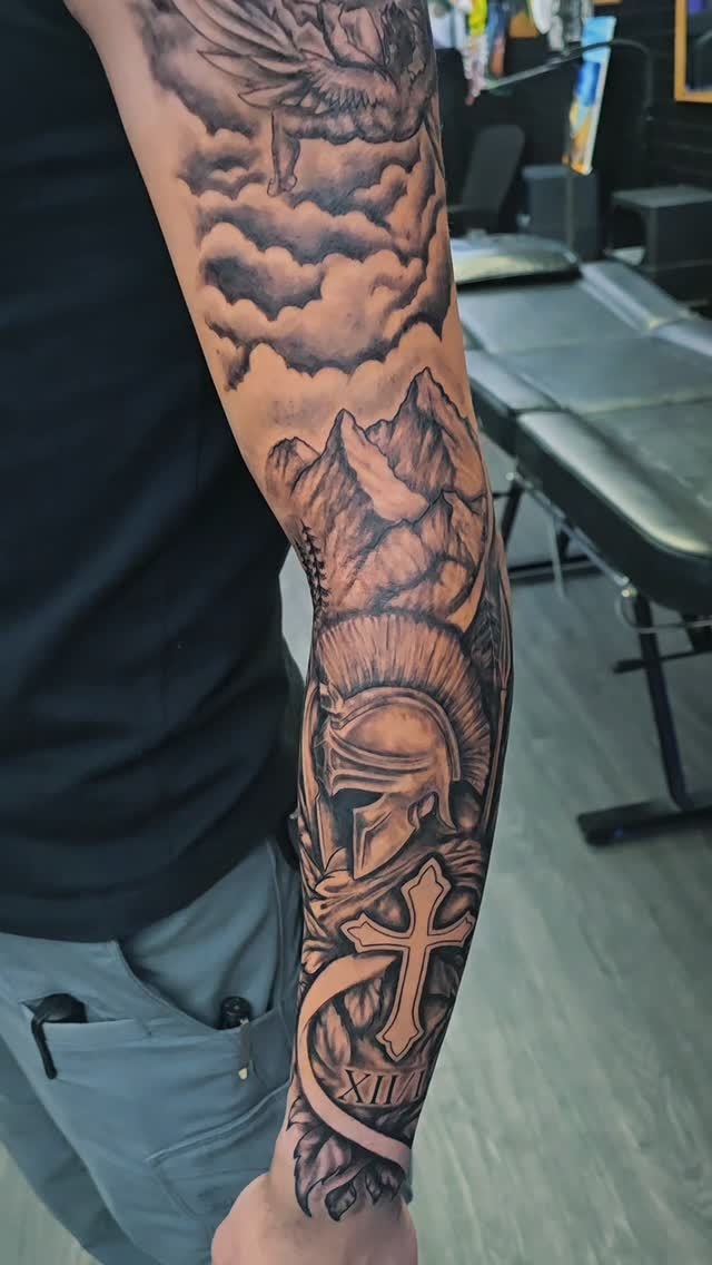 Tattoo by Angel at Z-Edge Gulf Gate: black and grey sleeve with a Spartan helmet, cross and mountains
